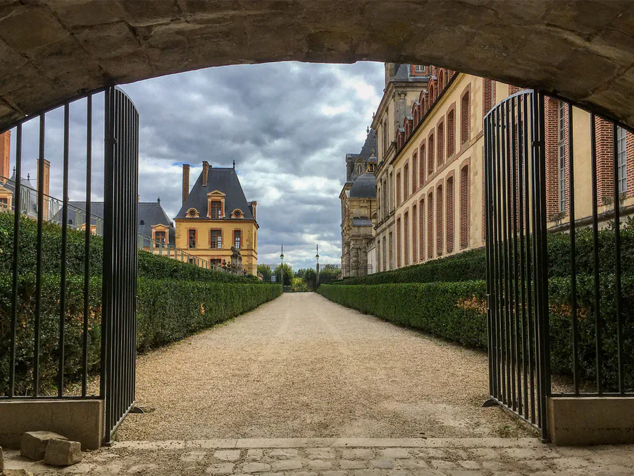 Après retouche : allée d’un château vue à travers une grille ouverte, ciel nuageux ravivé