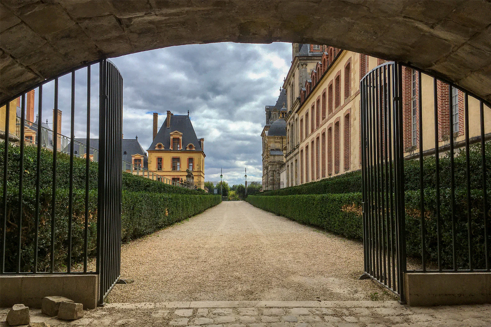 Après retouche : allée d’un château vue à travers une grille ouverte, ciel nuageux ravivé