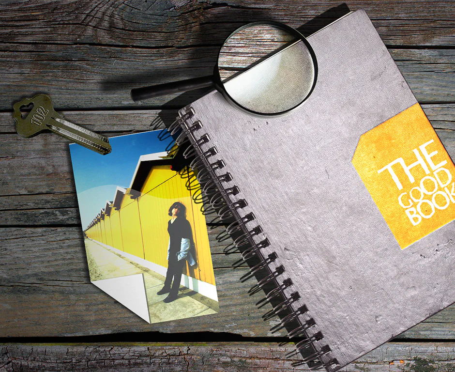 Photomontage « The Good Book » : carnet à spirale, loupe, clés et photo sur une table en bois