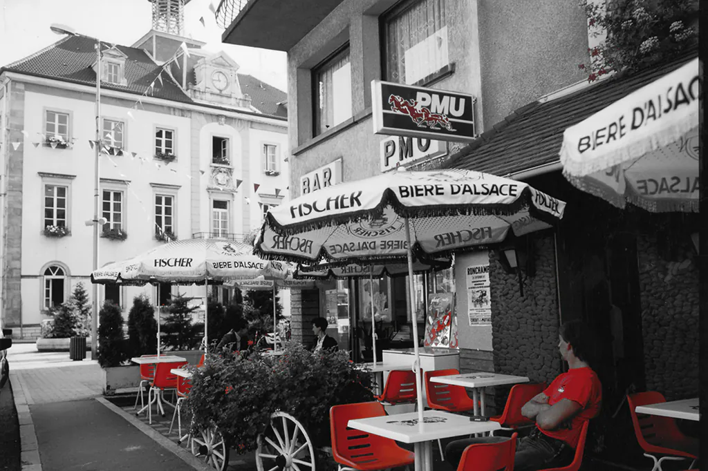 Après retouche : terrasse de café en noir et blanc, parasols et chaises rouges gardés en couleur